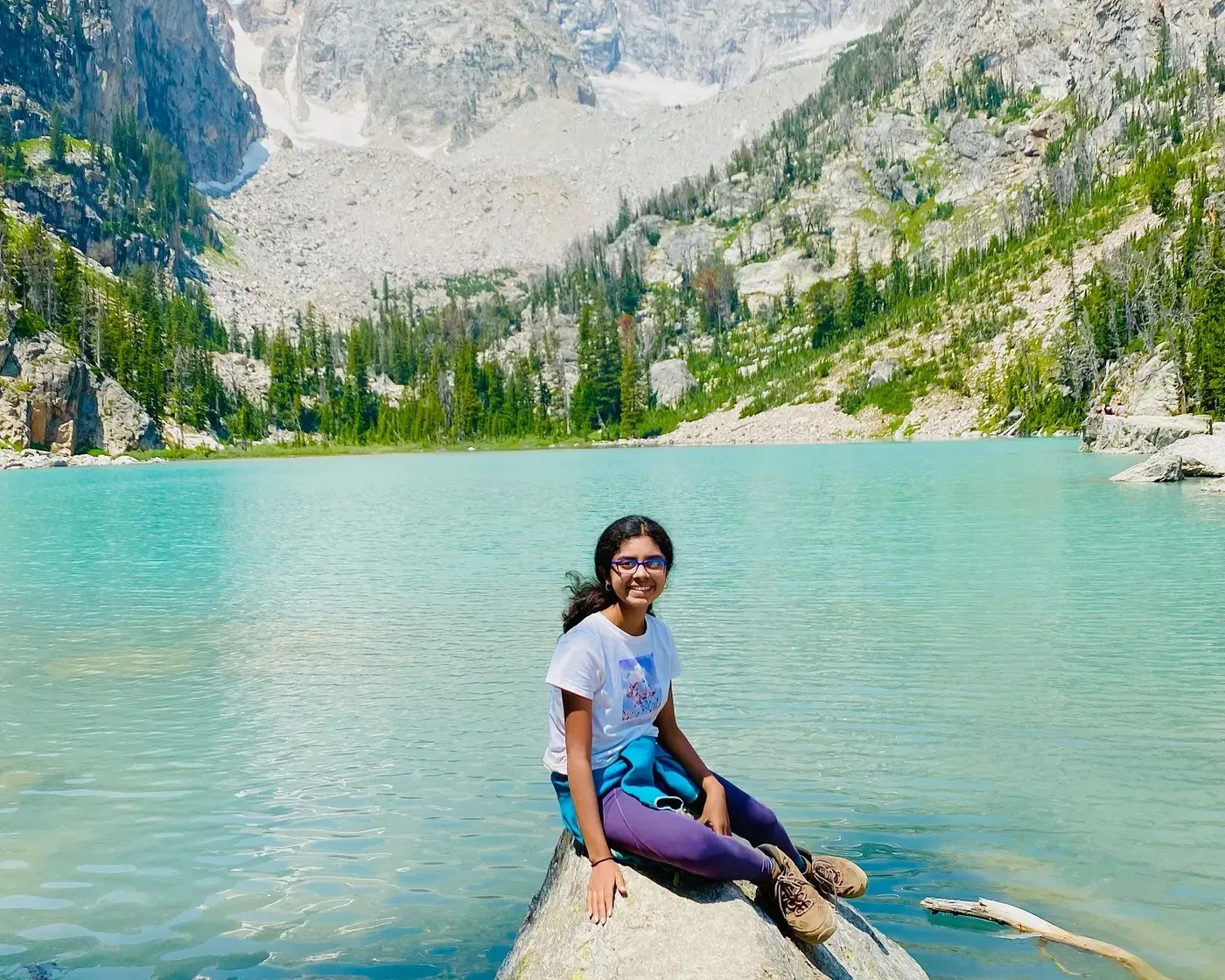 Ananya sitting on a large boulder in the turquoise water of Delta Lake