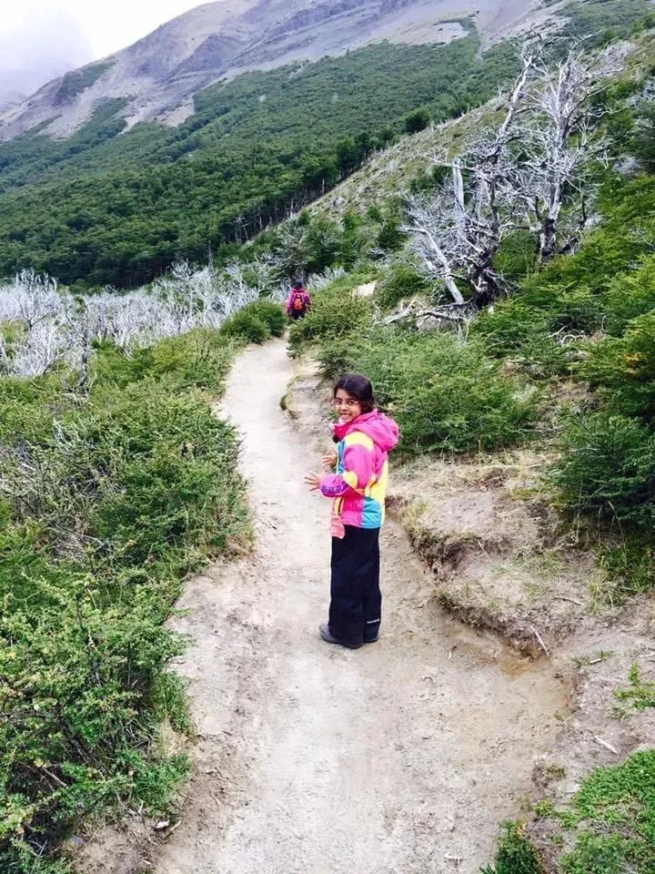 Ananya, aged six, in a pink and blue jacket on a sandy trail through low bushes