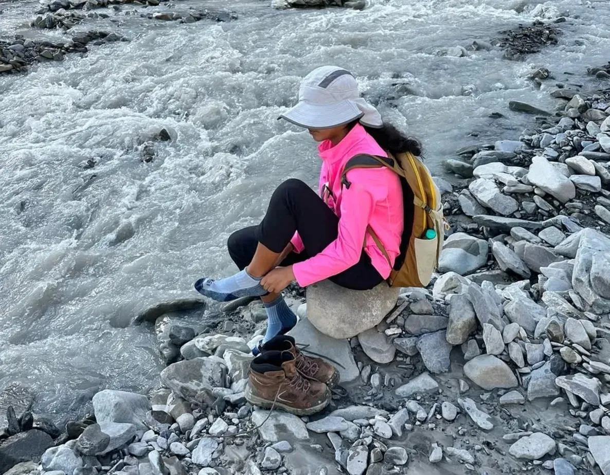 Ananya taking off her socks on the rocks beside the icy river