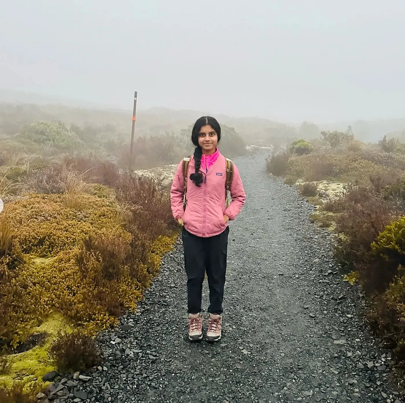 Ananya in a pink jacket on a misty gravel trail at dawn