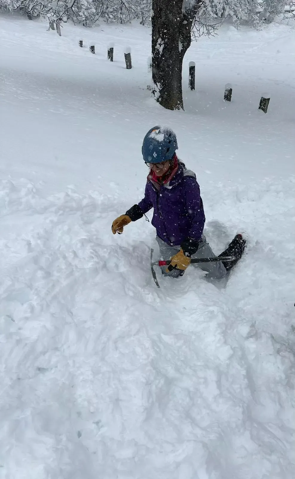 Ananya kneeling in deep snow, gripping an ice axe
