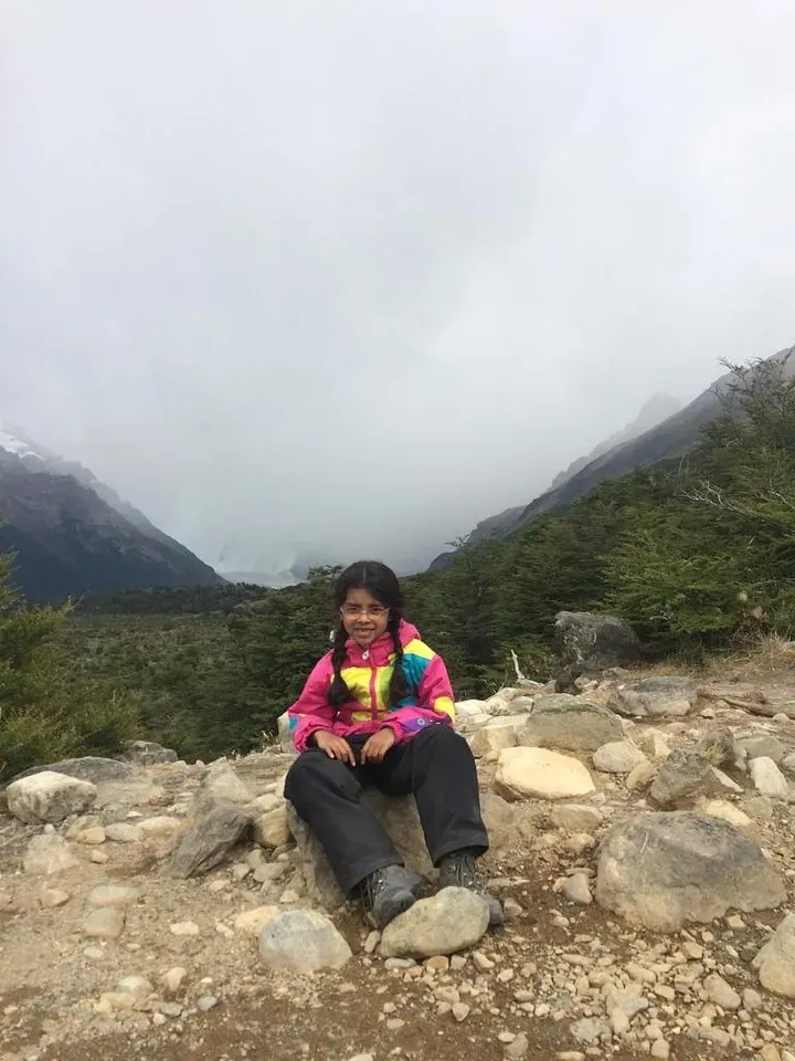 Ananya sitting on rocks at the top, smiling, with the Andes behind her