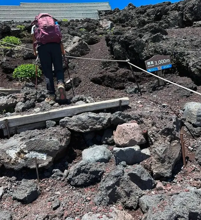 Ananya climbing past the 3,000 m altitude sign on dark volcanic rock