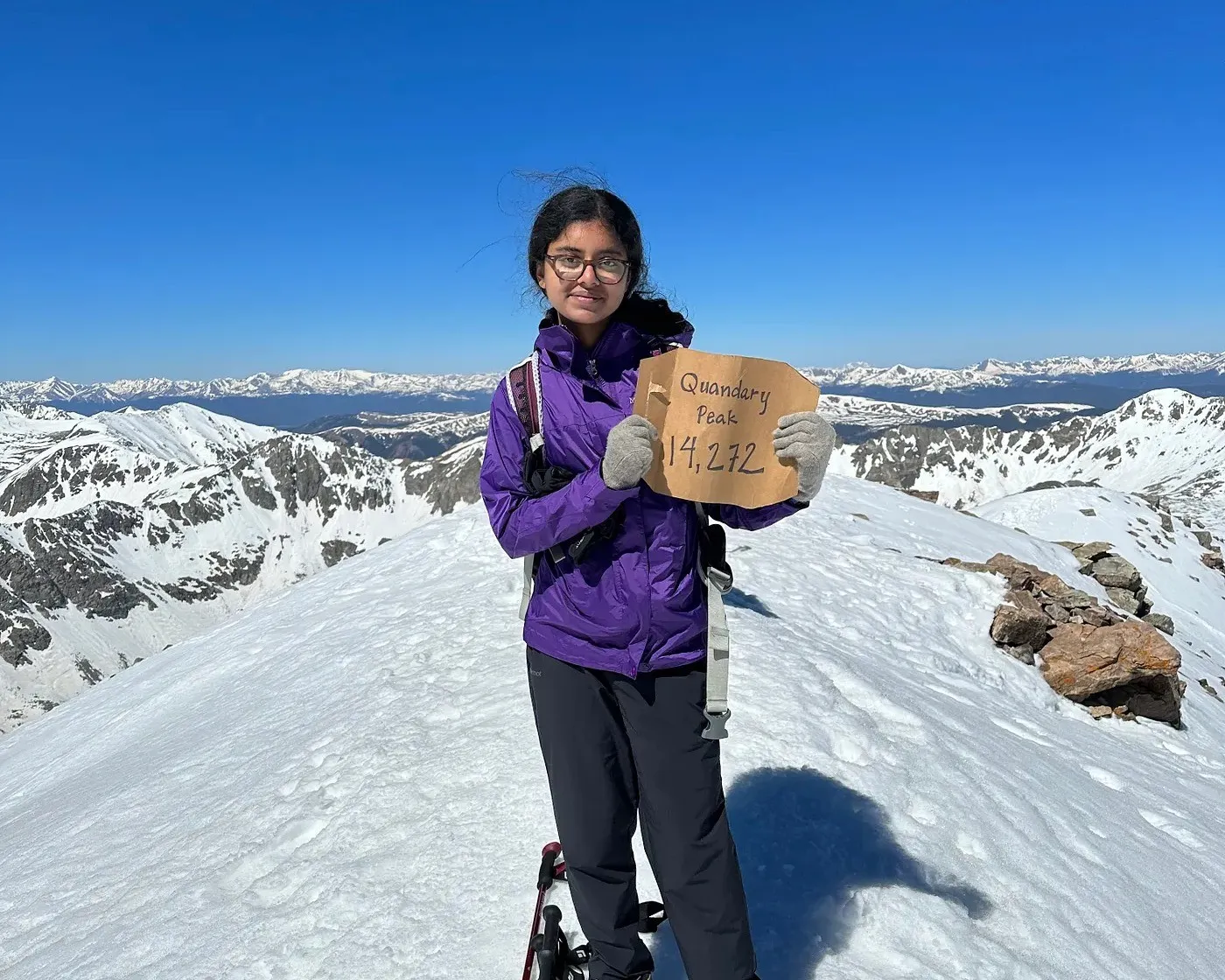 Ananya at the summit of Quandary Peak holding a sign reading Quandary Peak 14,272