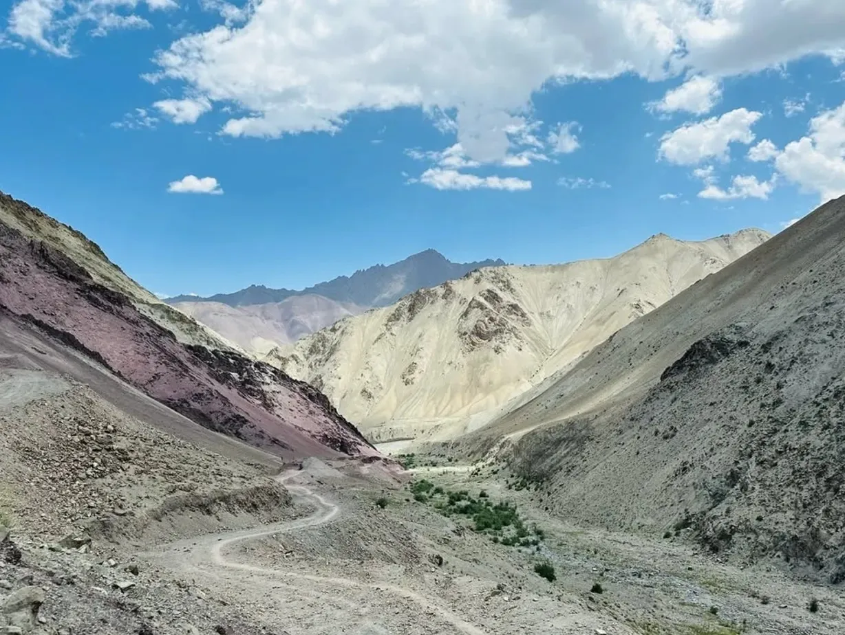 A dirt trail winding through a valley of red and pale mountains