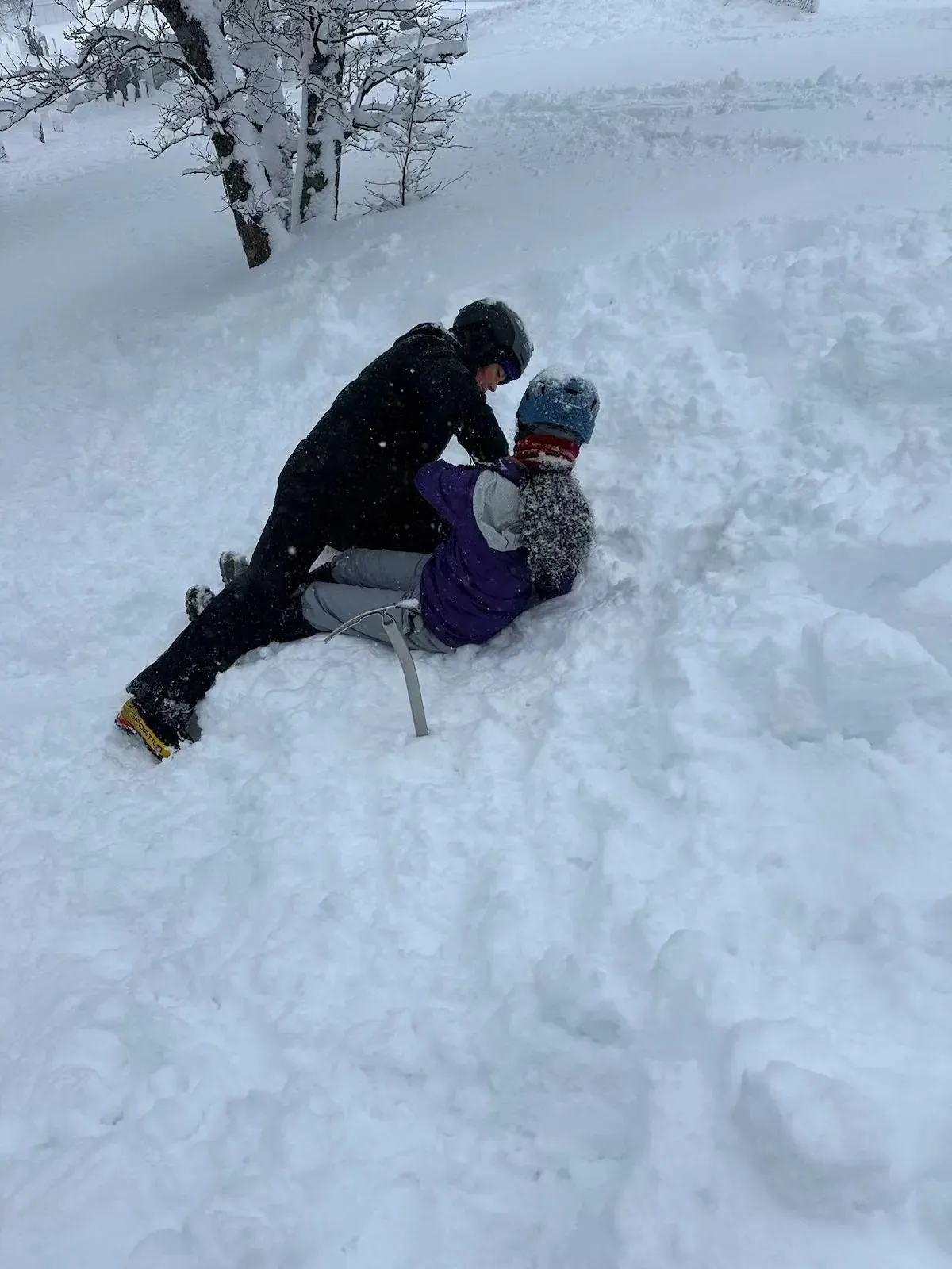 Beck helping Ananya practise sliding and stopping with an ice axe in fresh snow