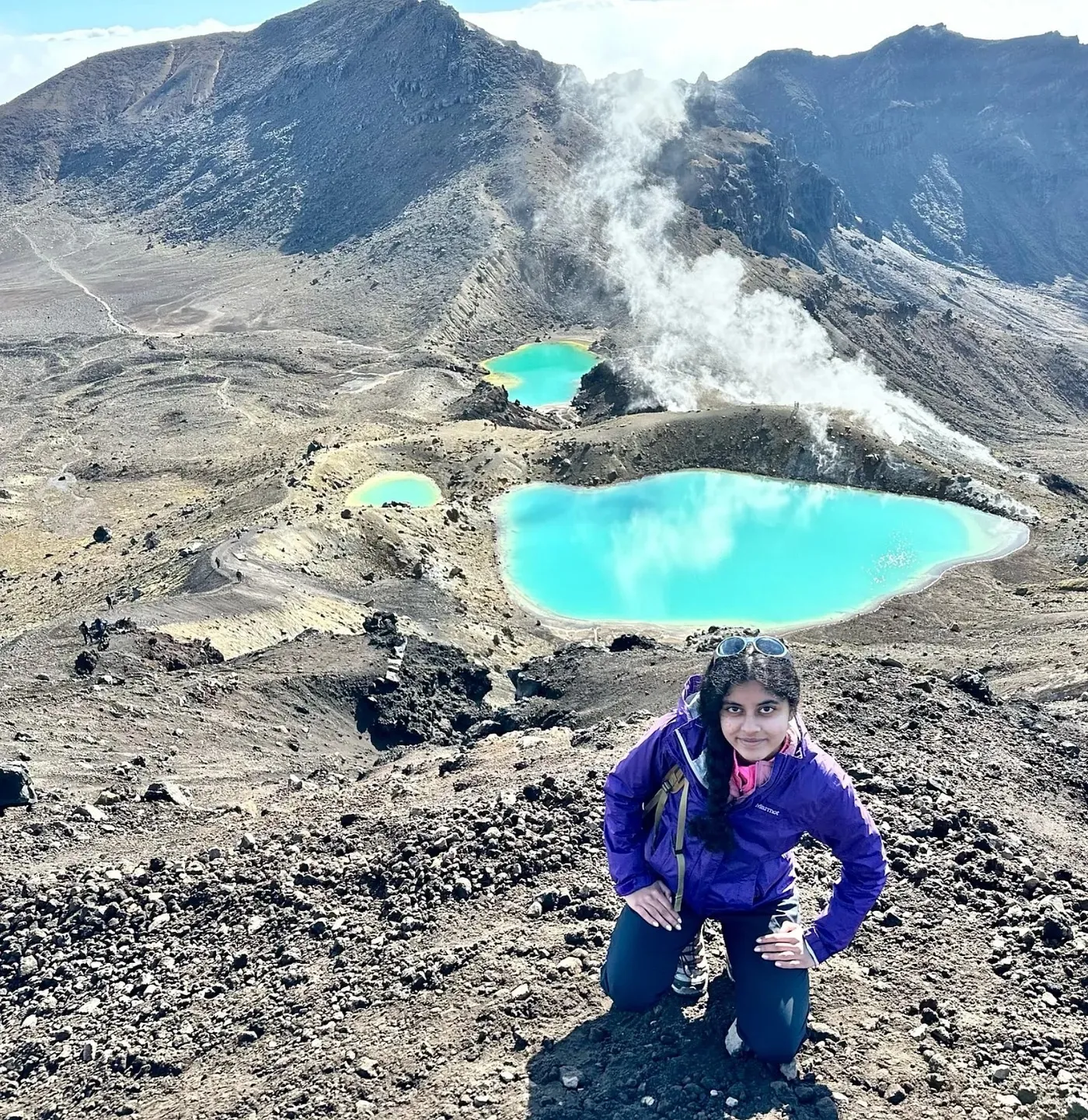 Ananya kneeling above the turquoise Emerald Lakes