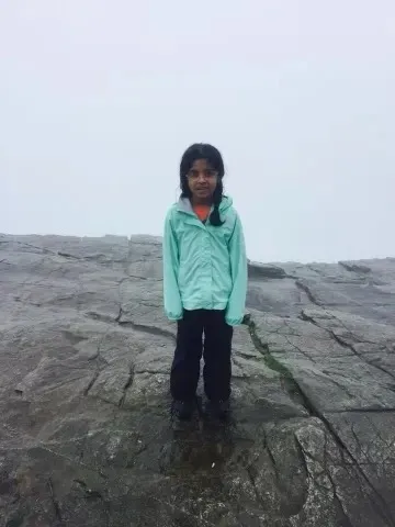 Ananya standing on the rock at the top of Pulpit Rock, wrapped in fog